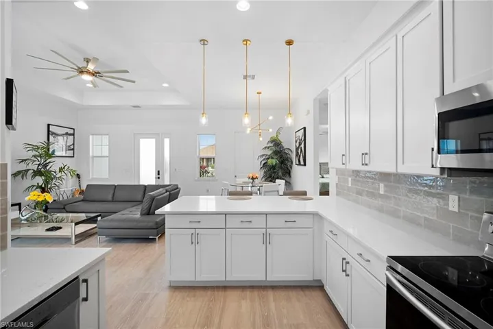 Kitchen with stainless steel appliances, white cabinets, light wood-style flooring, backsplash, and a raised ceiling