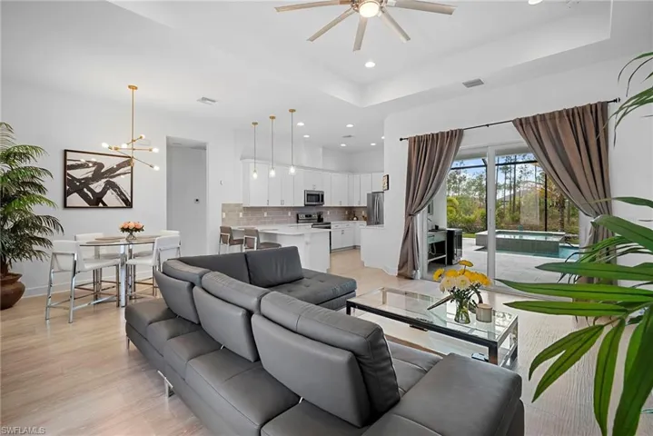 Living room featuring light wood-style flooring, a raised ceiling, a ceiling fan, and hanging lights