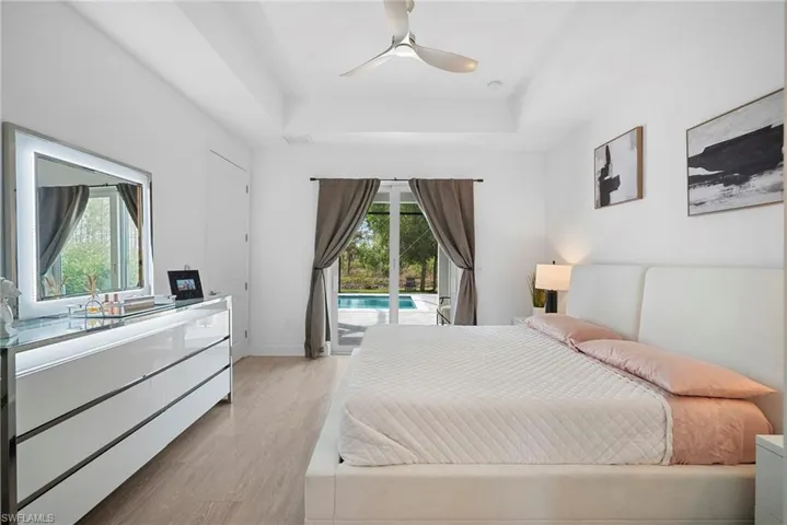 Bedroom with access to exterior, light wood-style floors, a ceiling fan, and a raised ceiling