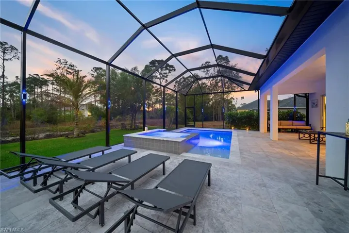 Pool at dusk featuring a sunroom, a patio, a lanai, a pool with connected hot tub, and a yard