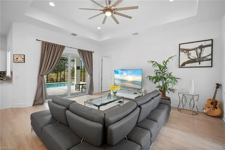 Living area featuring recessed lighting, ceiling fan, light wood-style floors, and a raised ceiling