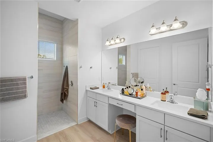 Bathroom featuring double vanity, walk in shower, and light wood-type flooring