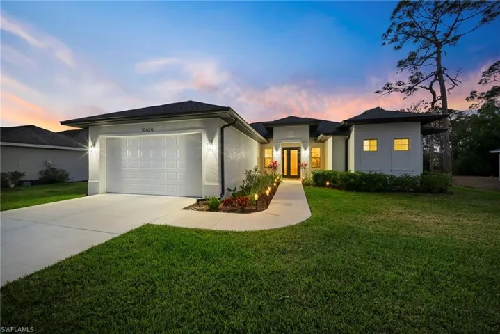 View of front of house featuring driveway, a lawn, stucco siding, and a garage