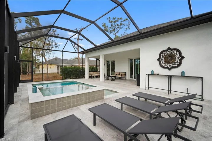 Outdoor pool featuring a patio area, a sunroom, glass enclosure, an in-ground hot tub, and an outdoor hangout area