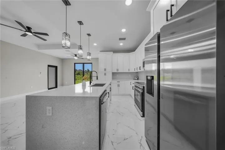 Modern kitchen featuring a large island with a light-toned countertop, white cabinetry with dark hardware, stainless steel appliances, and sleek pendant lighting