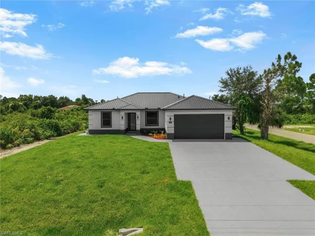 Contemporary single-story residence featuring a gray metal roof, attached garage, paved driveway, and manicured lawn