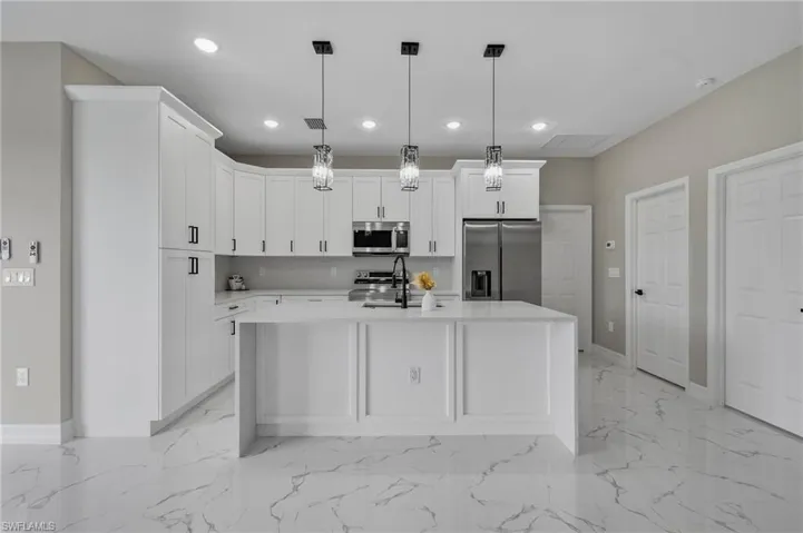 White shaker cabinetry with crown molding, stainless steel appliances, polished tile flooring, and an island with pendant lighting