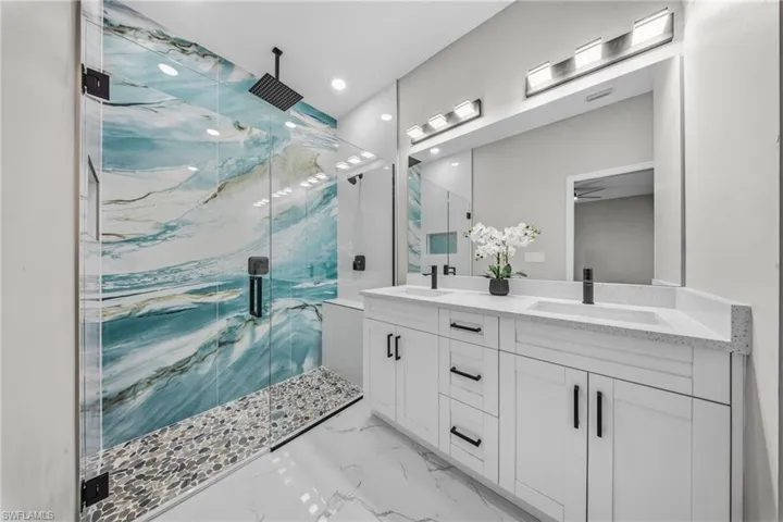 Glass-enclosed shower with abstract blue and white tile, pebble flooring, and a black rain showerhead