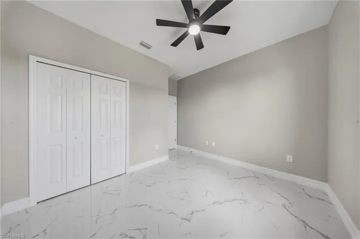 Spacious room featuring large format tile flooring, a contemporary black ceiling fan, white bi-fold closet doors, and light neutral wall paint