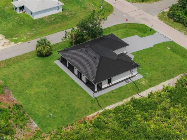 Modern construction with a dark metal roof, light-colored siding, covered patio, and concrete driveway
