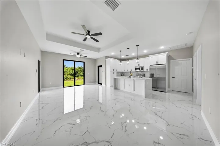 Open-concept living area with high ceilings, white marble-finish flooring, and a kitchen featuring white cabinetry and stainless steel appliances
