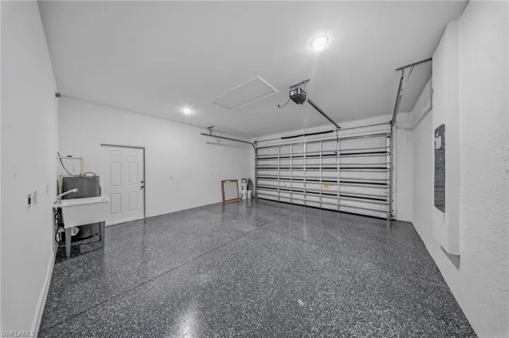 Attached two-car garage featuring a speckled epoxy floor finish, overhead lighting, and a utility sink