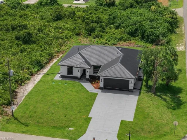 Modern exterior with dark gray metal roof, attached garage, concrete driveway, and manicured lawn