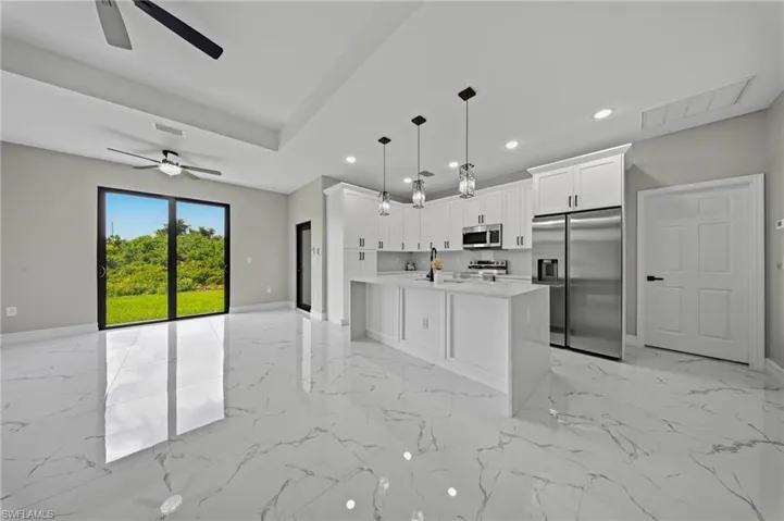 Open-concept living space featuring high ceilings, large format tile flooring, a kitchen island with pendant lighting, and stainless steel appliances