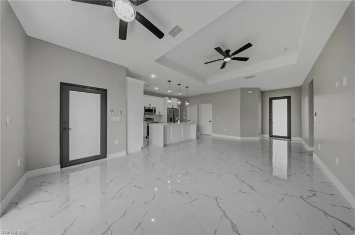 Open concept living space featuring large format porcelain tile flooring, contemporary ceiling fans, and tray ceilings