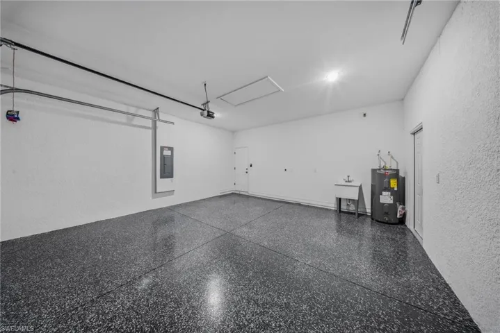 Spacious garage with textured walls, epoxy flooring, utility sink, and water heater