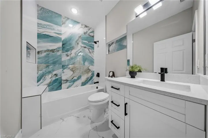 Built-in bathtub with a custom tiled surround, white vanity with an integrated sink, quartz countertop, and a large wall-mounted mirror