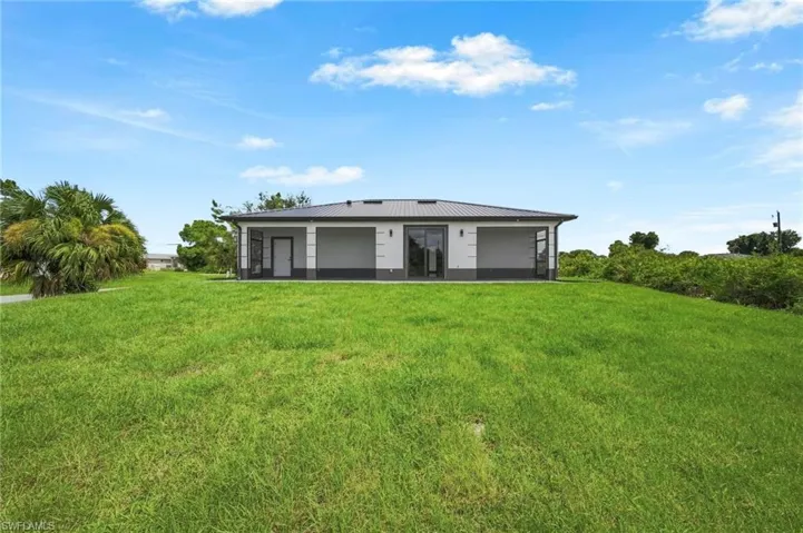 Spacious rear yard with a manicured lawn, modern exterior with a dark metal roof, screened patio areas, and multiple sliding glass doors