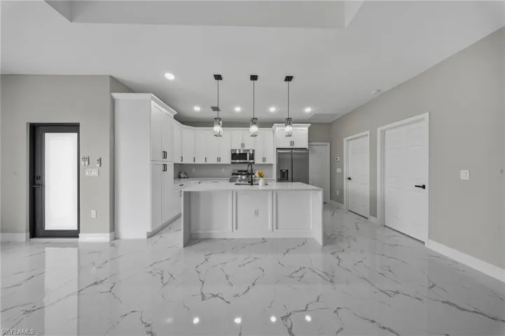 White shaker cabinetry with dark hardware, a kitchen island with pendant lighting, stainless steel appliances, and large format tile flooring