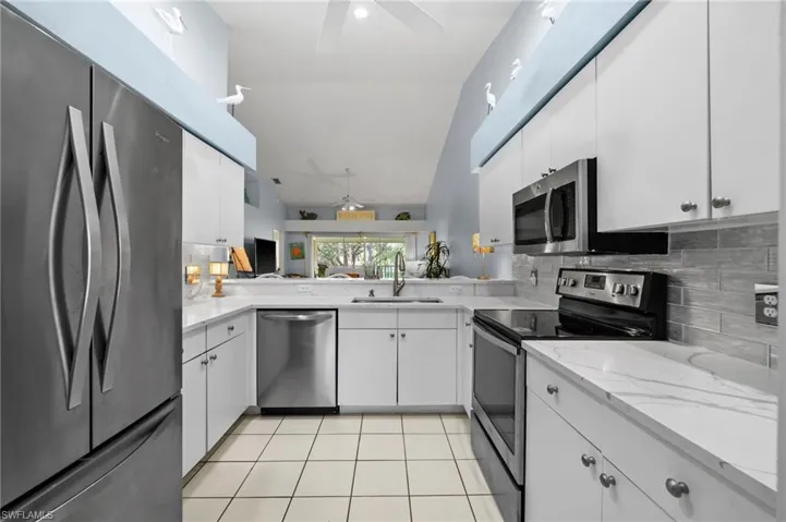 Kitchen with stainless steel appliances, ceiling fan, white cabinetry, backsplash, and lofted ceiling
