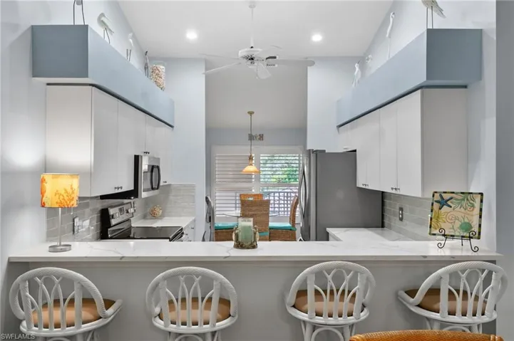 Kitchen featuring decorative backsplash, light stone counters, appliances with stainless steel finishes, and a high ceiling