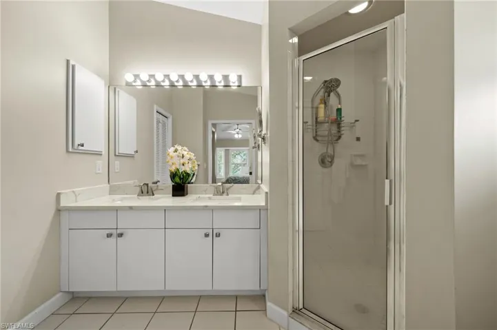 Bathroom featuring a shower stall, light tile patterned floors, double vanity, and a ceiling fan