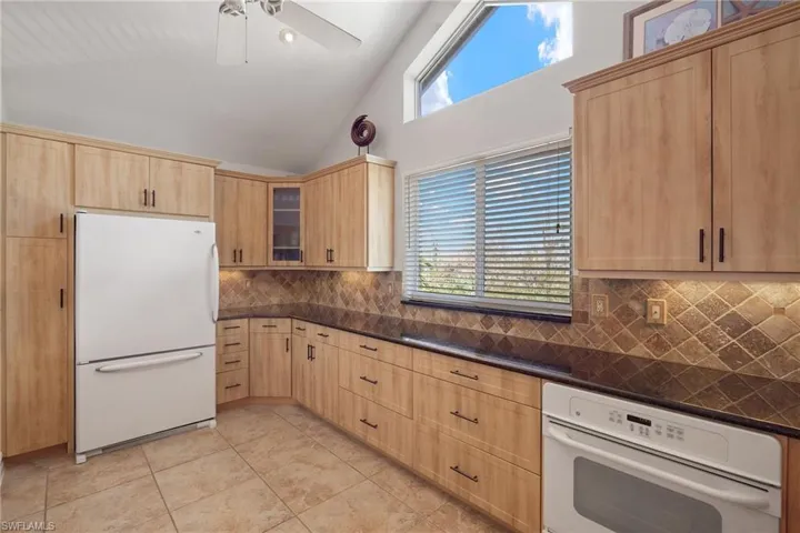 Kitchen featuring white appliances, light brown cabinets, glass insert cabinets, backsplash, and high vaulted ceiling