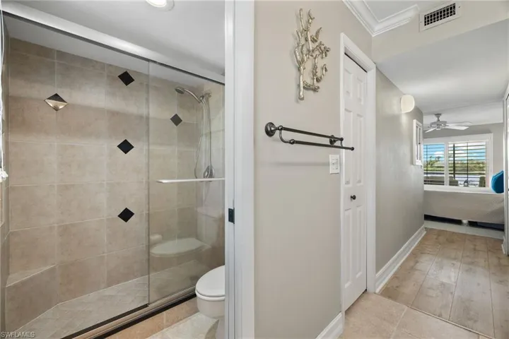Ensuite bathroom featuring a ceiling fan, ornamental molding, a stall shower, and light tile patterned flooring