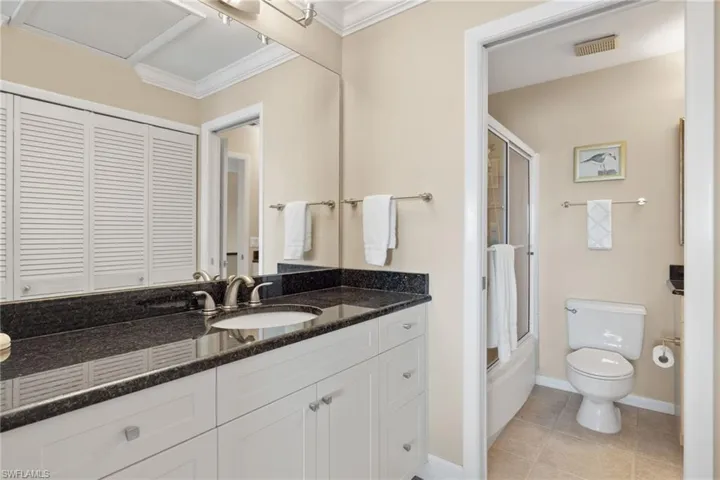 Full bathroom featuring vanity, light tile patterned flooring, combined bath / shower with glass door, crown molding, and a closet