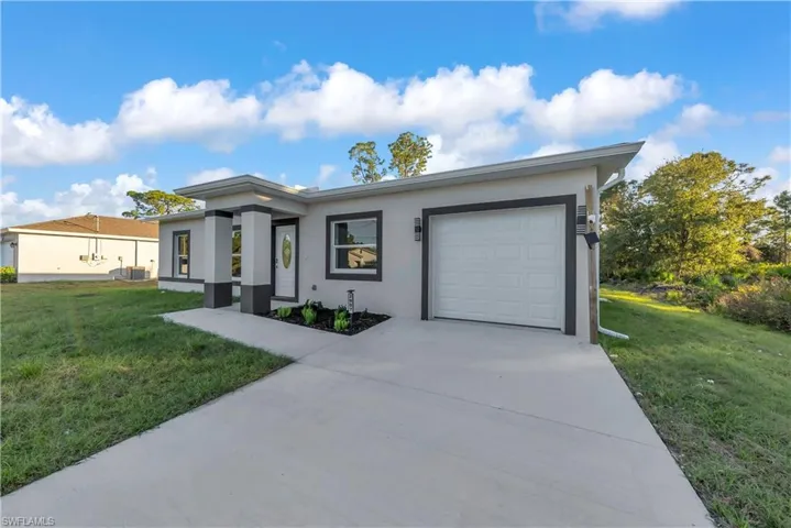 View of front of property featuring a front yard, stucco siding, an attached garage, and driveway