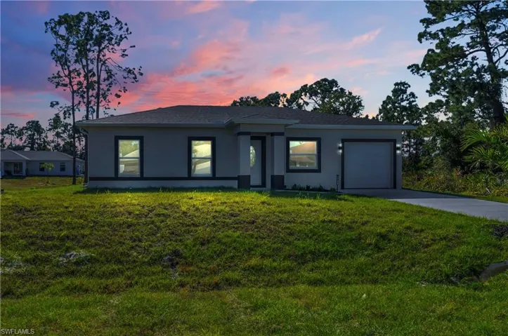 Prairie-style house featuring an attached garage, driveway, stucco siding, and a yard
