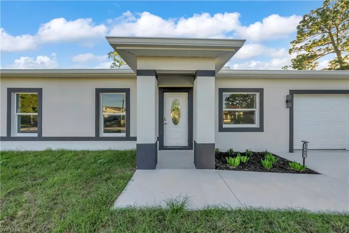 View of exterior entry with stucco siding, an attached garage, and a yard