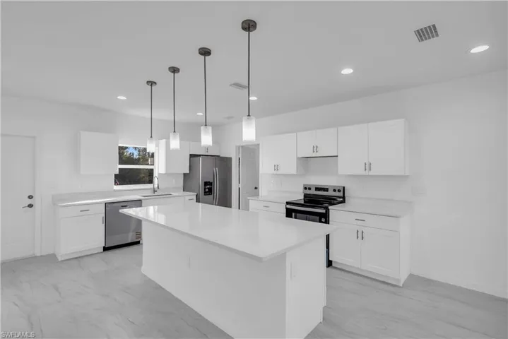 Kitchen with white cabinets, appliances with stainless steel finishes, decorative light fixtures, a center island, and recessed lighting