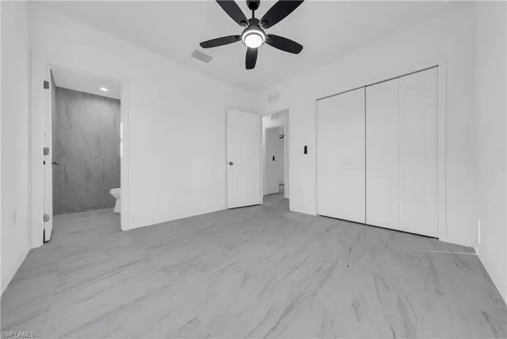 Unfurnished bedroom featuring a ceiling fan, a closet, light marble finish flooring, and ensuite bathroom