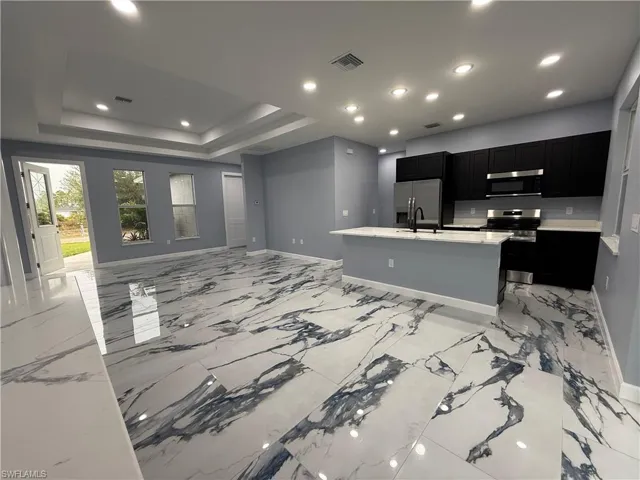Kitchen with sink, a tray ceiling, stainless steel appliances, light stone countertops, and a kitchen island with sink