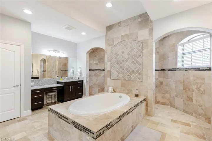 Bathroom with vanity, a garden tub, a walk in shower, light stone finish floors, and recessed lighting