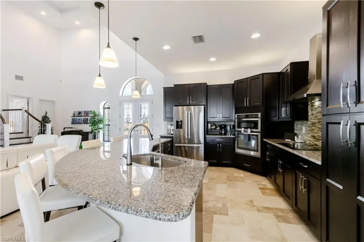 Kitchen featuring stainless steel appliances, hanging light fixtures, light stone countertops, tasteful backsplash, and light stone finish floors