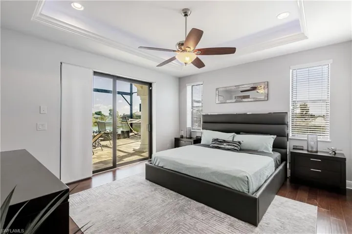 Bedroom with dark wood-style floors, a tray ceiling, access to exterior, ceiling fan, and recessed lighting