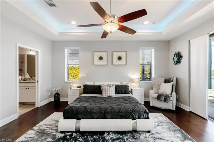 Bedroom featuring access to exterior, dark wood finished floors, a tray ceiling, ceiling fan, and ensuite bathroom