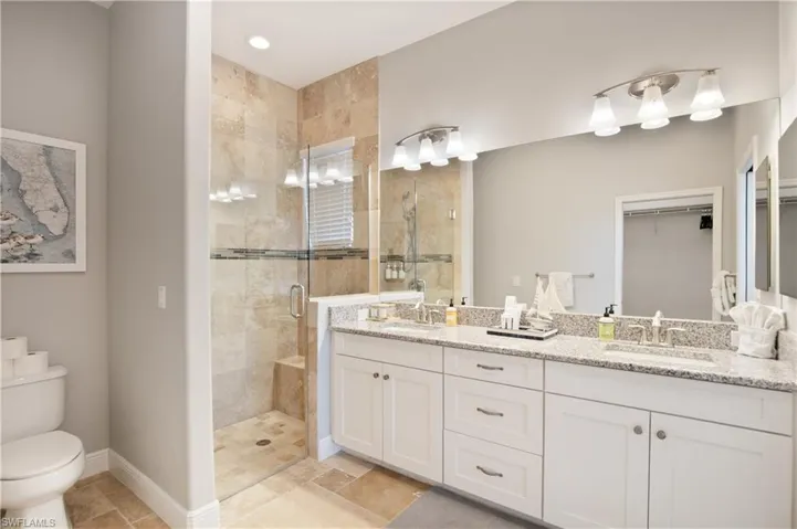 Full bathroom with double vanity, a stall shower, a spacious closet, and light stone finish flooring