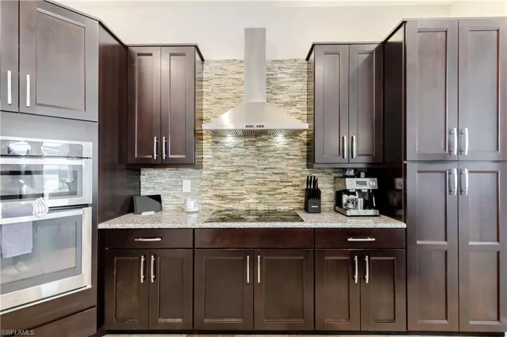 Kitchen featuring double oven, light stone countertops, dark wood finish cabinets, black gas cooktop, and backsplash
