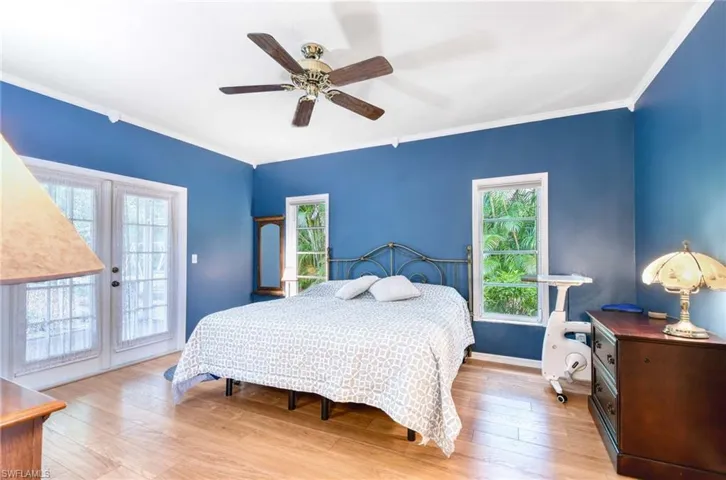 Bedroom with access to outside, multiple windows, wood finished floors, and ornamental molding