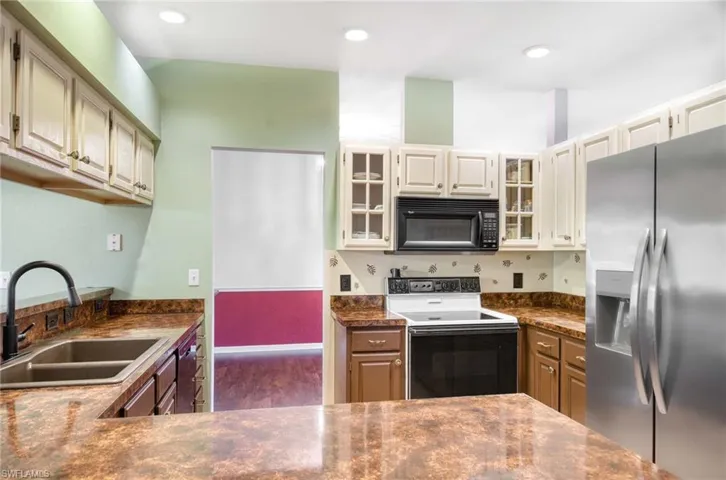 Kitchen with stainless steel fridge with ice dispenser, black microwave, electric range oven, a sink, and dark countertops