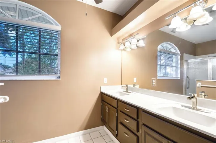 Bathroom featuring a shower stall, tile patterned floors, double vanity, ceiling fan, and baseboards