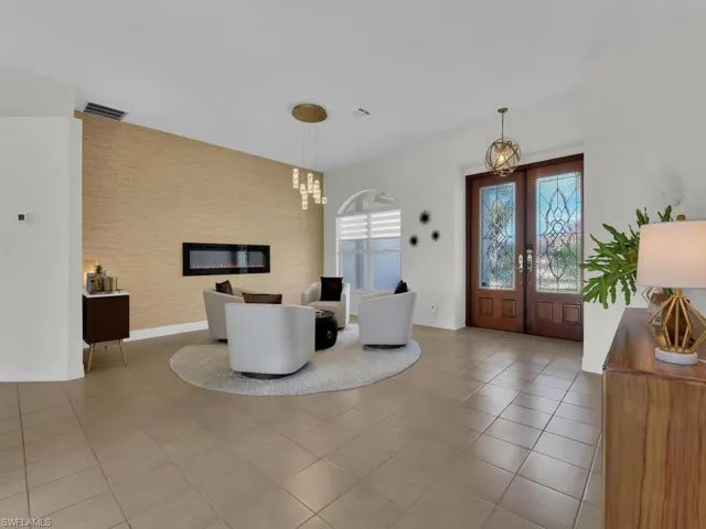 Entryway featuring french doors, a chandelier, a glass covered fireplace, light tile patterned flooring, and an accent wall