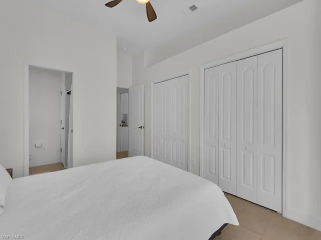 Bedroom with multiple closets, light tile patterned floors, and ceiling fan