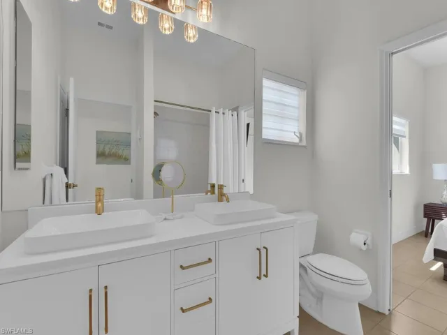 Ensuite bathroom featuring double vanity, light tile patterned floors, and a shower with curtain