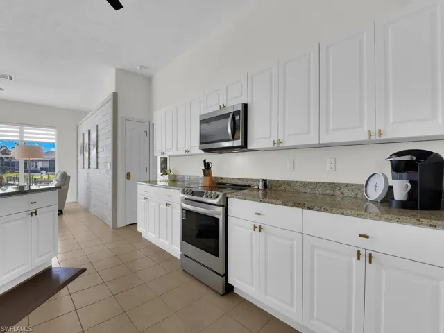 Kitchen with white cabinets, stainless steel appliances, dark stone countertops, and light tile patterned floors