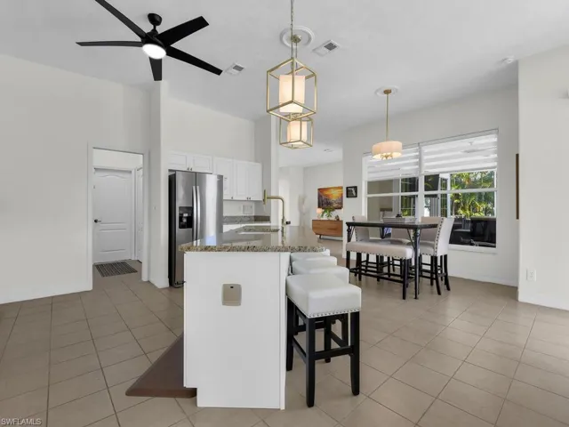 Kitchen featuring white cabinets, a kitchen breakfast bar, stainless steel refrigerator with ice dispenser, a ceiling fan, and decorative light fixtures