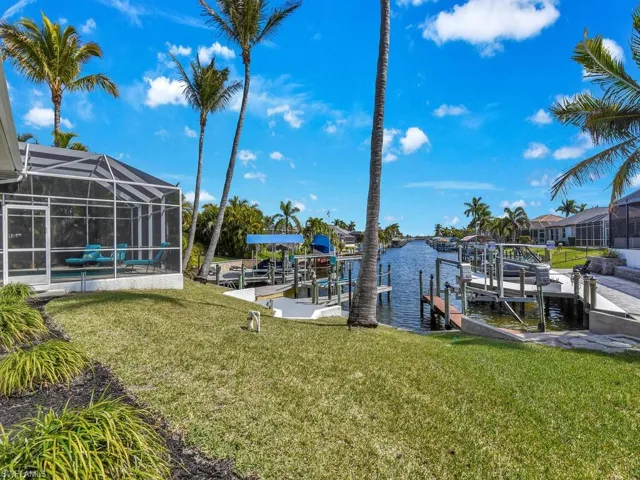 Dock area with a sunroom, boat lift, a yard, a water view, and glass enclosure